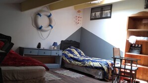 Een slaapkamer met een bed, een bureau, een stoel, een houten boekenkast, een aan de muur bevestigd reddingsboei en een stadsgezicht poster.