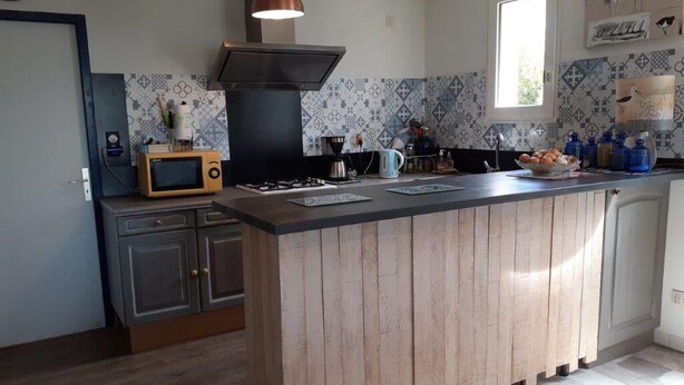 Een keuken met een centraal kookeiland, een magnetron, een fornuis en een koffiezetapparaat.