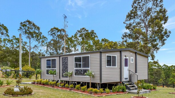 A single-story mobile home with a flat roof, a front porch, and a small front yard with various plants. - Wallaby Gully Farm Cottage Peace, Quiet, Serenity (Ellalong)