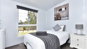 A bedroom with a bed, bedside table, lamp, and a painting on the wall. - Wallaby Gully Farm Cottage Peace, Quiet, Serenity (Ellalong)