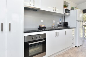 A modern kitchen with white cabinetry, a built-in oven, a microwave, and a coffee machine. - Wallaby Gully Farm Cottage Peace, Quiet, Serenity (Ellalong)