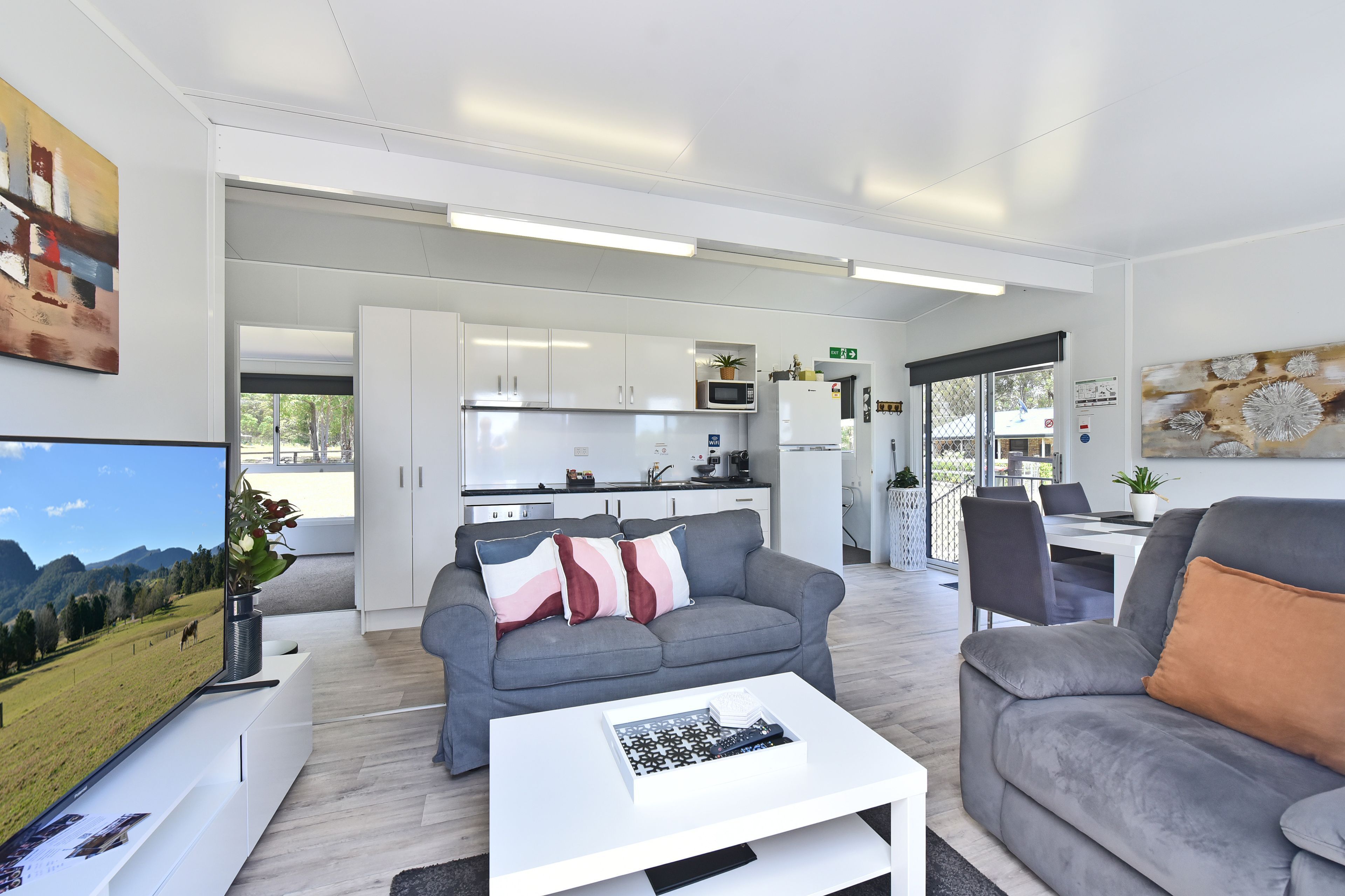 A modern living room with a grey sofa, a white coffee table, and a dining area with a table and chairs.