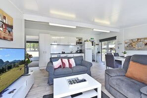 A modern living room with a grey sofa, a white coffee table, and a dining area with a table and chairs. - Wallaby Gully Farm Cottage Peace, Quiet, Serenity (Ellalong)