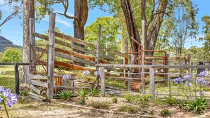 A rustic wooden fence with a metal gate, surrounded by trees and purple flowers. - Wallaby Gully Farm Cottage Peace, Quiet, Serenity (Ellalong)