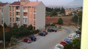 En boligbygning med flere etager og altaner, omgivet af parkerede biler og grøntområder.