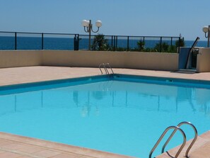 Une piscine rectangulaire dotée d’une plage carrelée, de rampes métalliques et d’une clôture.