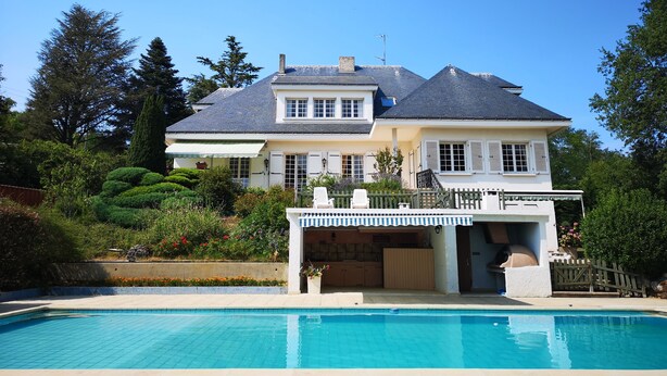 En stor bolig med swimmingpool, overdækket terrasse og en velholdt have.