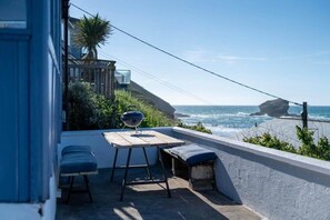 A balcony with a table and chairs, overlooking the ocean with a rocky outcrop in the distance. - Beach House with Stunning Sea Views (Portreath)