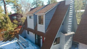 Una casa con techo pronunciado, un porche con barandilla y un patio cubierto de nieve.
