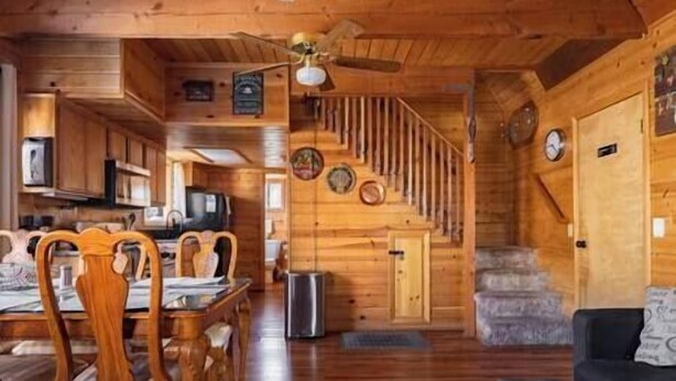 Interior de una cabaña de madera con comedor, cocina, escalera y sala de estar.