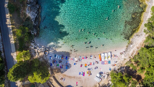 An aerial view of a beach with clear turquoise water, a sandy shore, and people sunbathing and swimming. - Villa grotta istriana mit neu pool near center and Arena in Pula (Pula)