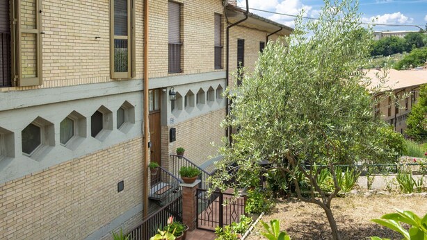 A two-story building with a brick facade, a balcony with a metal railing, and a garden with various plants and a tree. - Small villa near the historic center with free parking (Assisi)