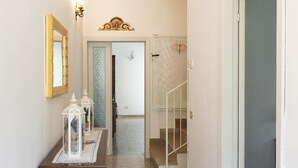 A hallway with a wooden cabinet, a mirror, and two white lanterns on a table. A staircase with a white railing is visible in the background. - Small villa near the historic center with free parking (Assisi)