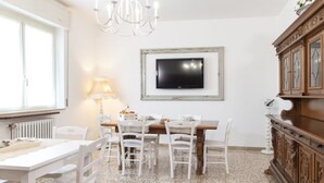 A dining area with a white table, chairs, a chandelier, a television, and a wooden cabinet. - Small villa near the historic center with free parking (Assisi)