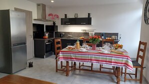 Eine kompakte Küche mit Kühlschrank, Backofen und Spüle. Ein Esstisch mit Stühlen ist mit Frühstücksartikeln gedeckt.