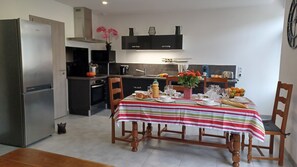 Cocina compacta con refrigerador, horno y pileta. Se prepara una mesa de comedor con sillas, servida con alimentos para el desayuno.