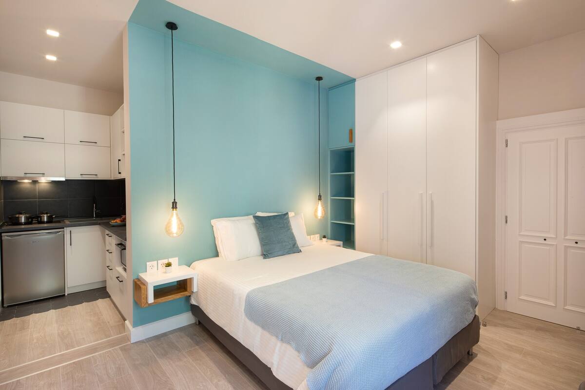 A modern bedroom with a bed, bedside tables, a built-in wardrobe, and a kitchen area.