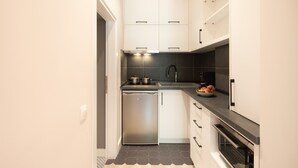 A compact kitchen with white cabinets, a dishwasher, a built-in oven, and a black countertop. - Corfu Town Twin Studios by CorfuEscapes (Corfu)