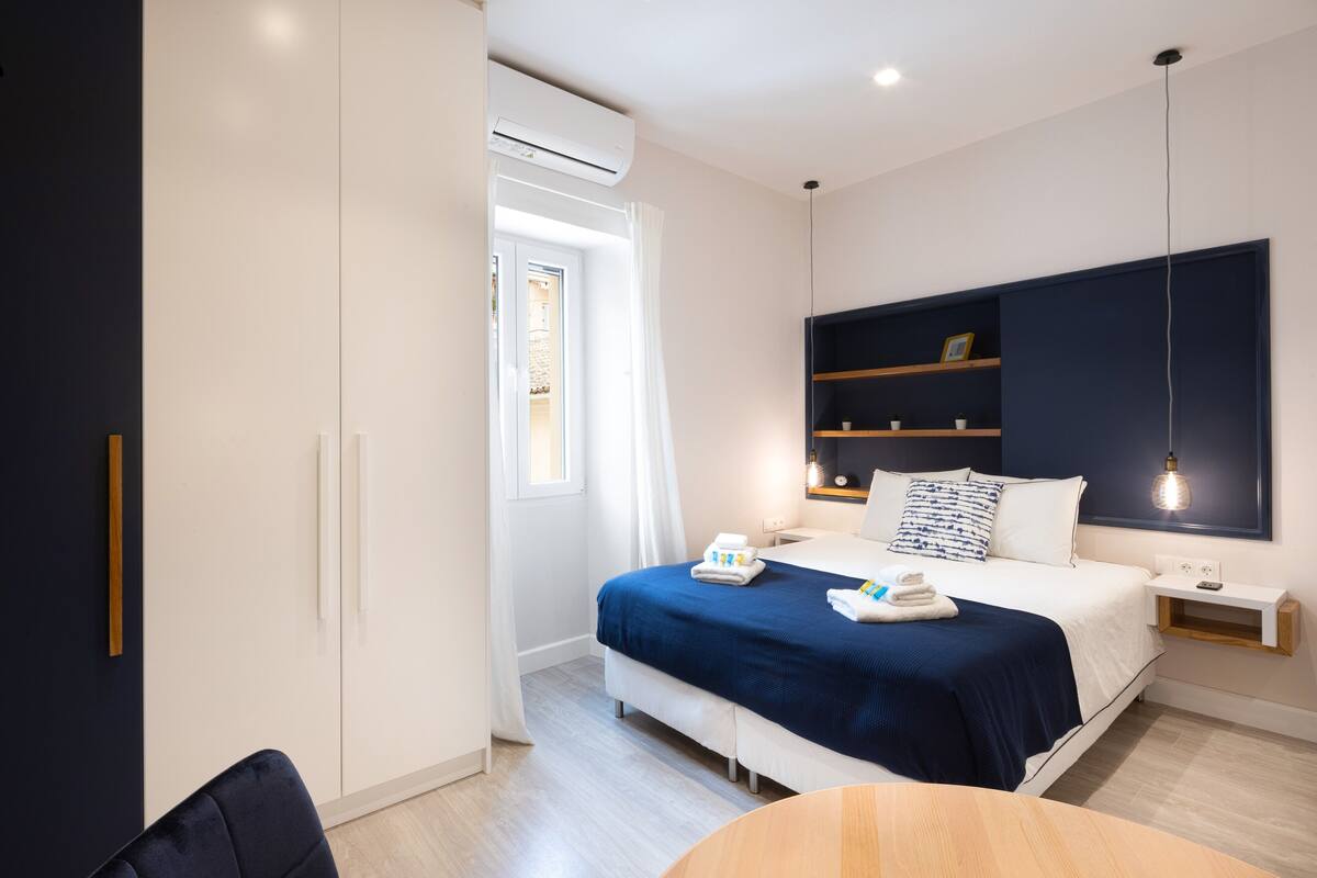 A modern hotel room with a bed, bedside tables, a wardrobe, and a window with curtains.
