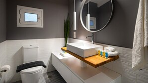 A modern bathroom with a white toilet, a rectangular sink with a wooden countertop, a round mirror, and a towel rack. - Corfu Town Twin Studios by CorfuEscapes (Corfu)
