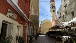 A narrow street with buildings on either side, a clock tower in the distance, and outdoor seating areas with umbrellas. - Corfu Town Twin Studios by CorfuEscapes (Corfu)
