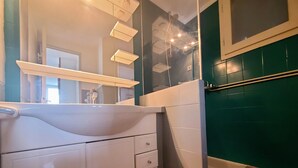 A bathroom with a white sink, a mirror, a shower, and a green tiled wall.