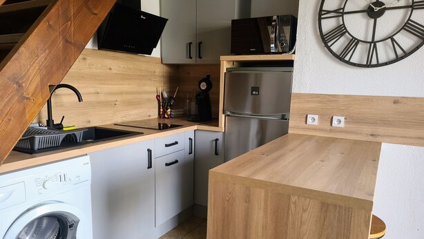 A compact kitchen with wooden cabinets, a stainless steel refrigerator, a microwave, and a sink.
