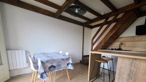 A compact kitchen with a dining area, featuring a wooden ceiling, a table with chairs, a small bar area, and a washing machine.