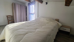A bedroom with a large bed, a wooden chair, a nightstand, and a window with curtains.