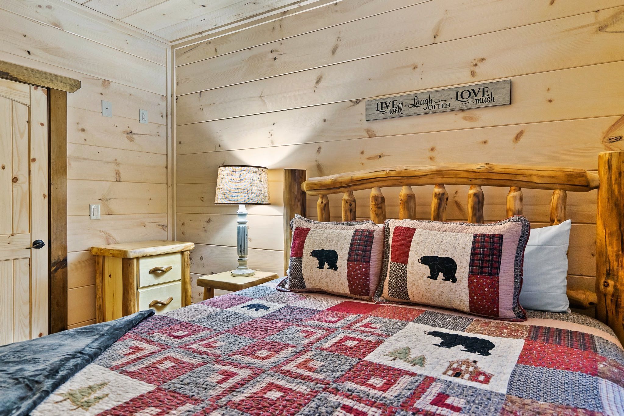 A wooden bedroom with a bed, a nightstand, a lamp, and a sign on the wall.