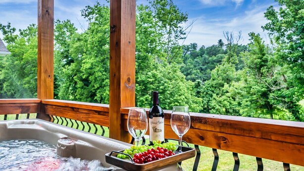 Un bain à remous avec un plateau de raisins, deux verres à vin, une bouteille de vin et une balustrade en bois donnant sur une forêt.