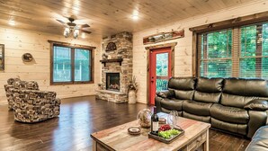 Un salon chaleureux avec une cheminée en pierre, un canapé en cuir et une table basse en bois sur laquelle sont disposés des en-cas.