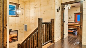 Un intérieur en bois avec un escalier en bois, un tableau accroché au mur et une porte donnant sur une autre pièce.