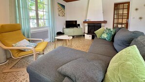 Un salon avec un canapé, un fauteuil jaune, une télévision, une cheminée et une fenêtre avec des rideaux.