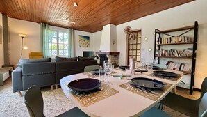 Un coin repas avec une table dressée pour quatre personnes, un canapé, une bibliothèque et une cheminée.