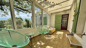 Une pièce lumineuse, baignée de soleil, avec de grandes fenêtres, une porte verte et une petite table entourée de chaises.