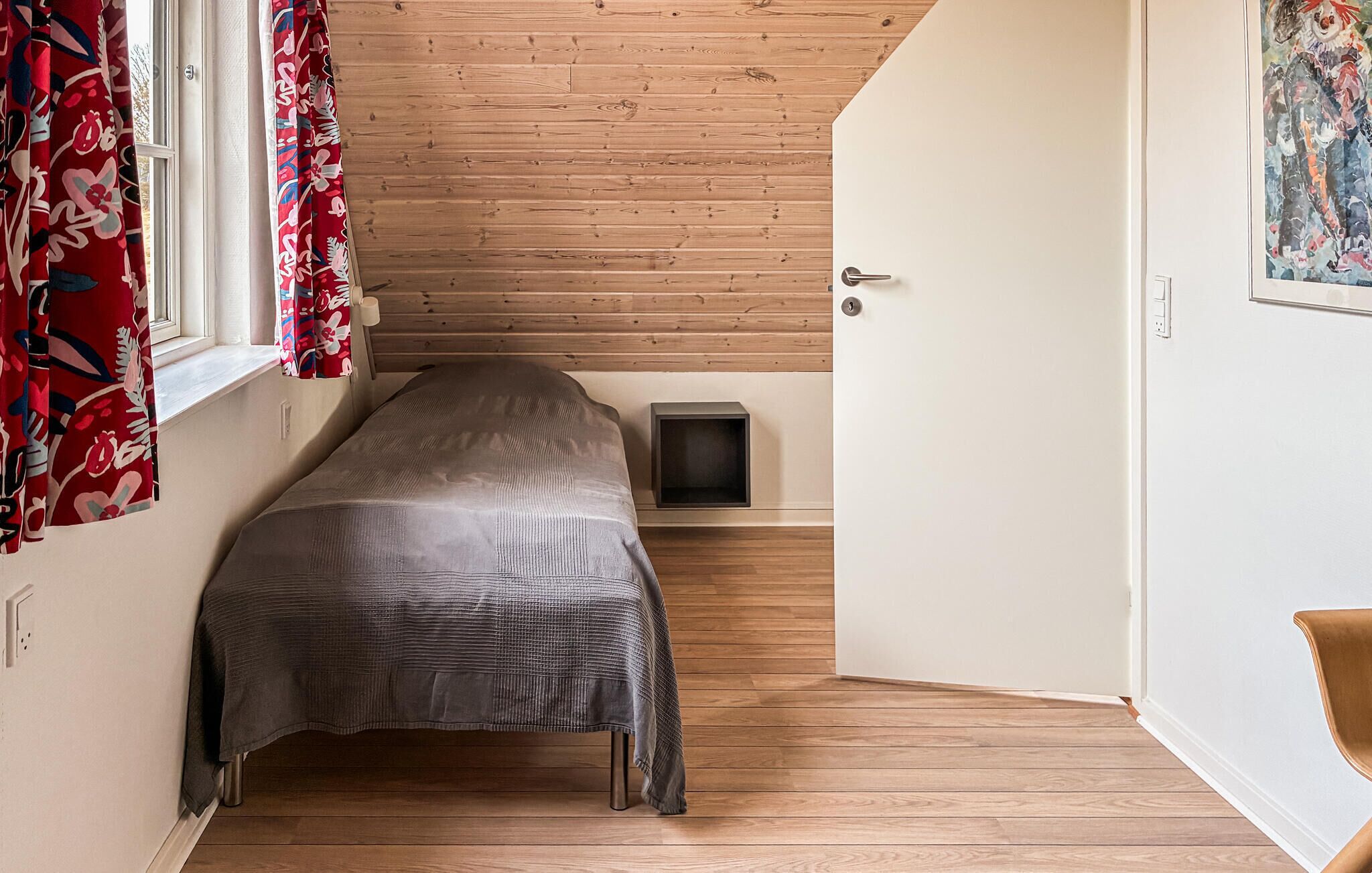 Een kleine kamer met een bed, een nachtkastje en een deur naar een andere kamer.