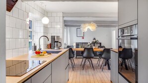 Una cocina moderna con azulejos blancos, una máquina de café y un comedor con sillas negras.