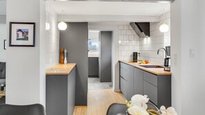 Una cocina moderna con armarios grises, una encimera de madera y un horno empotrado. Se ve un área de comedor con una mesa y sillas al fondo.