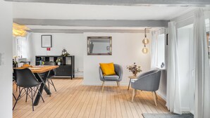 Un comedor moderno con una mesa de madera, sillas negras y un sillón gris con cojín amarillo.