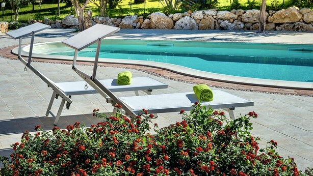 A poolside area with lounge chairs and a stone wall.