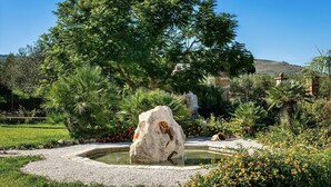 A garden with a rock formation, a pond, and various plants.