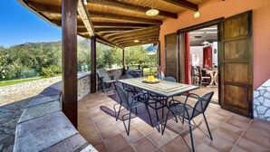 An outdoor patio with a wooden pergola, a table with chairs, and a stone wall.