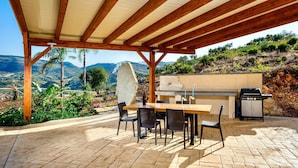 An outdoor patio with a wooden pergola, a table with chairs, a grill, and a view of a mountainous landscape. - Villa Luisa - Scopello (Scopello)