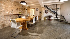 A dining area with a wooden table and white chairs, a stone wall, and a staircase with a metal railing. - Villa Luisa - Scopello (Scopello)