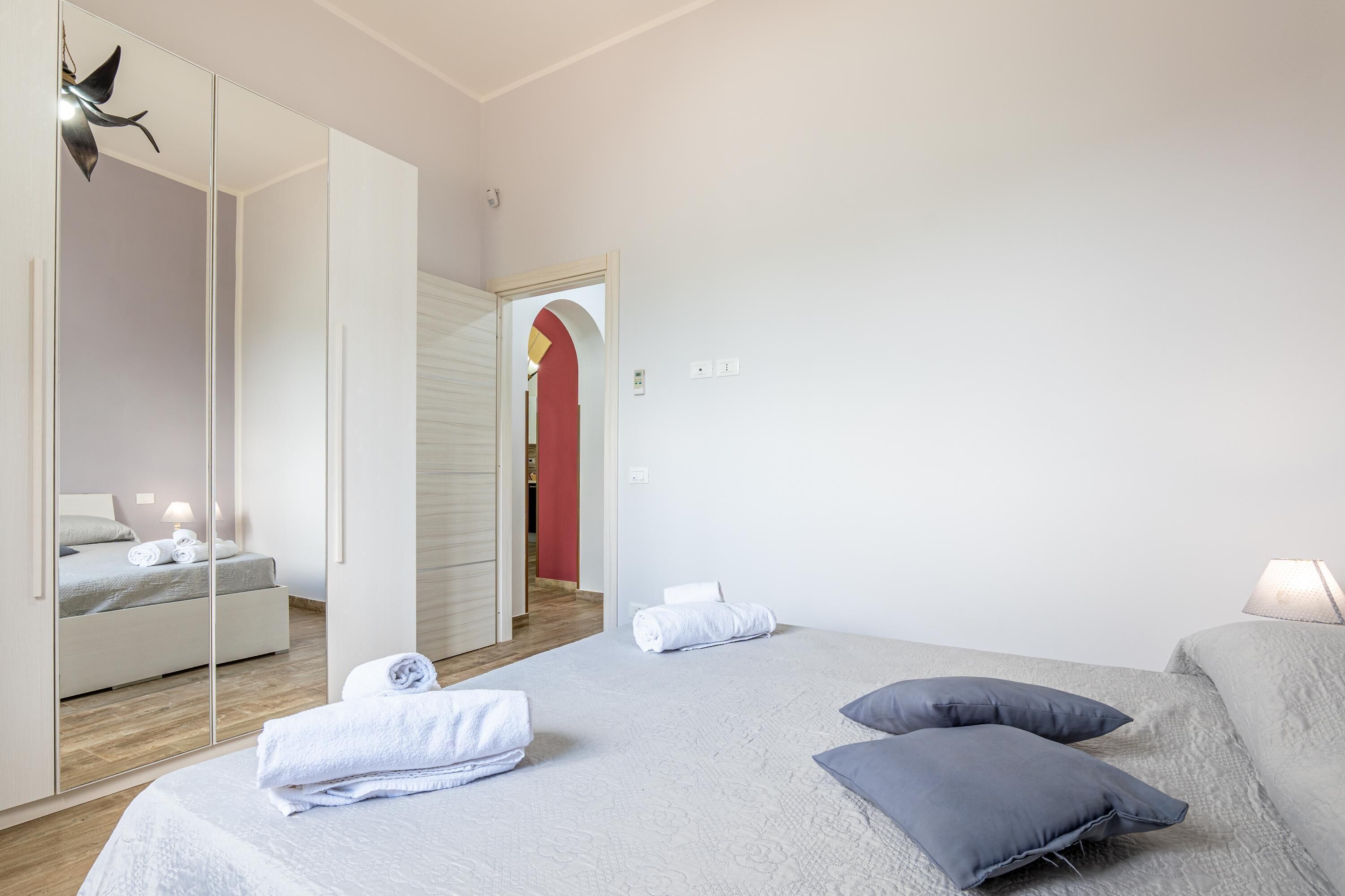 Una habitación de hotel con cama, espejo, puerta y un pasillo.