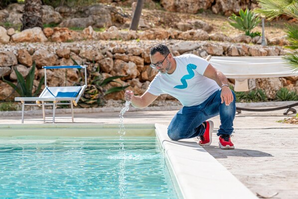 A man by a pool with clear water, a lounge chair, and a rocky background.