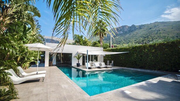 A modern pool area with lounge chairs and a covered seating area, surrounded by lush greenery and a mountain backdrop. - Villa Marianna - Terrasini (Terrasini)