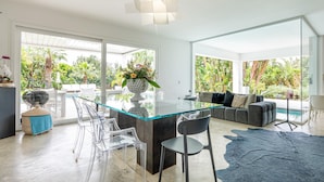 A modern kitchen with a glass island, clear chairs, a sofa, and a view of a pool and garden. - Villa Marianna - Terrasini (Terrasini)