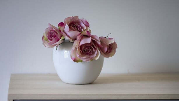 Een witte dressoir met drie lades en een vaas met roze rozen erop.
